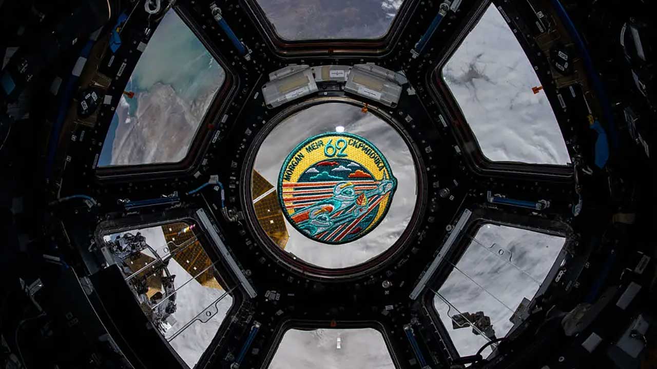 Feb. 21, 2020) — The Expedition 62 mission patch floats inside the seven-window cupola, the International Space Station’s “window to the world.” The orbiting complex was flying 265 miles above Russia near the Caspian Sea at the time this photograph was taken.