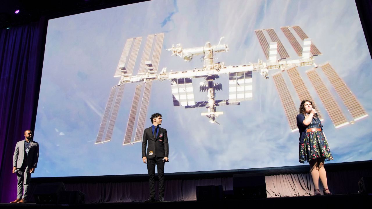 Broadway Broadway performers sing in front of space station backdrop.