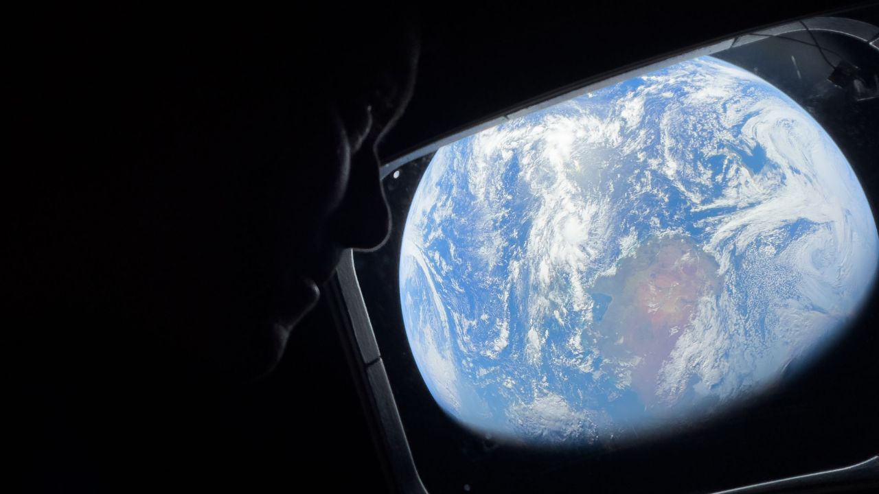 NASA astronaut and Artemis II Commander Reid Wiseman peers out of one of the Orion spacecraft's main cabin windows, looking back at Earth, as the crew travels towards the Moon.