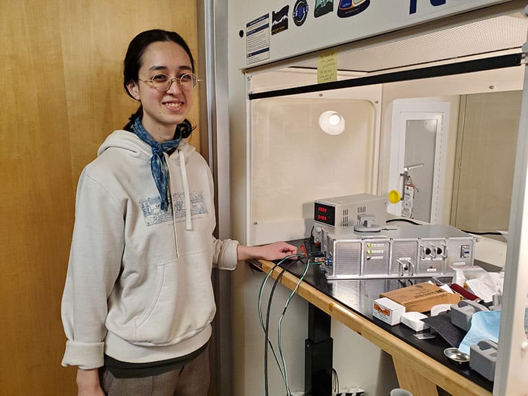 Upward-9_2-ELVIS-Nikki-Johnston Nikki Johnston, a Ph.D. student at Portland State University, stands next to the Extant Life Volumetric Imaging System (ELVIS). This innovative system aims to advance how we study cellular processes in space.