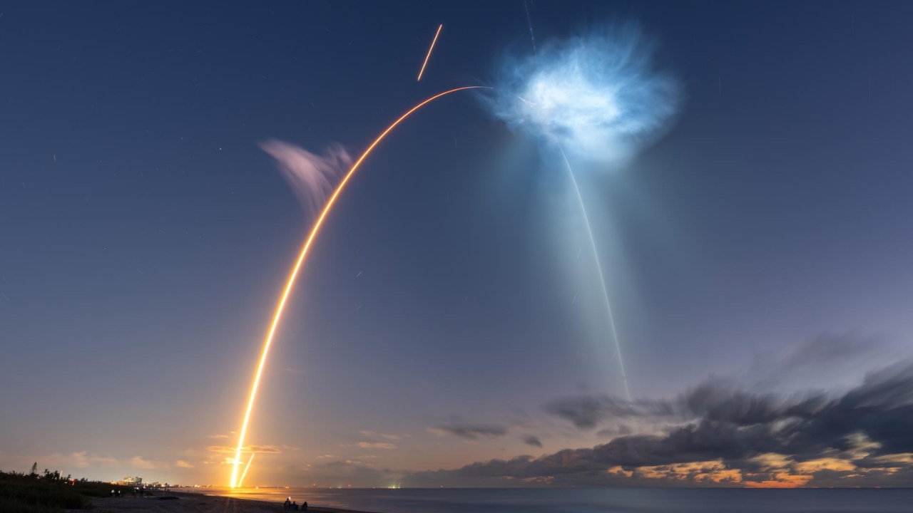 Long-exposure view of SpaceX CRS-35 launching to the International Space Station, with the Falcon 9’s sunlit exhaust plume streaking across the predawn sky as the booster returns to land.